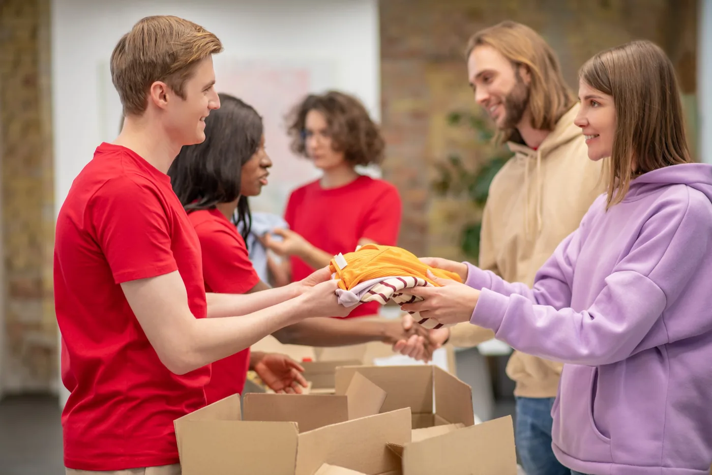 Volunteers in red shirts handing folded clothing across a table of cardboard boxes.