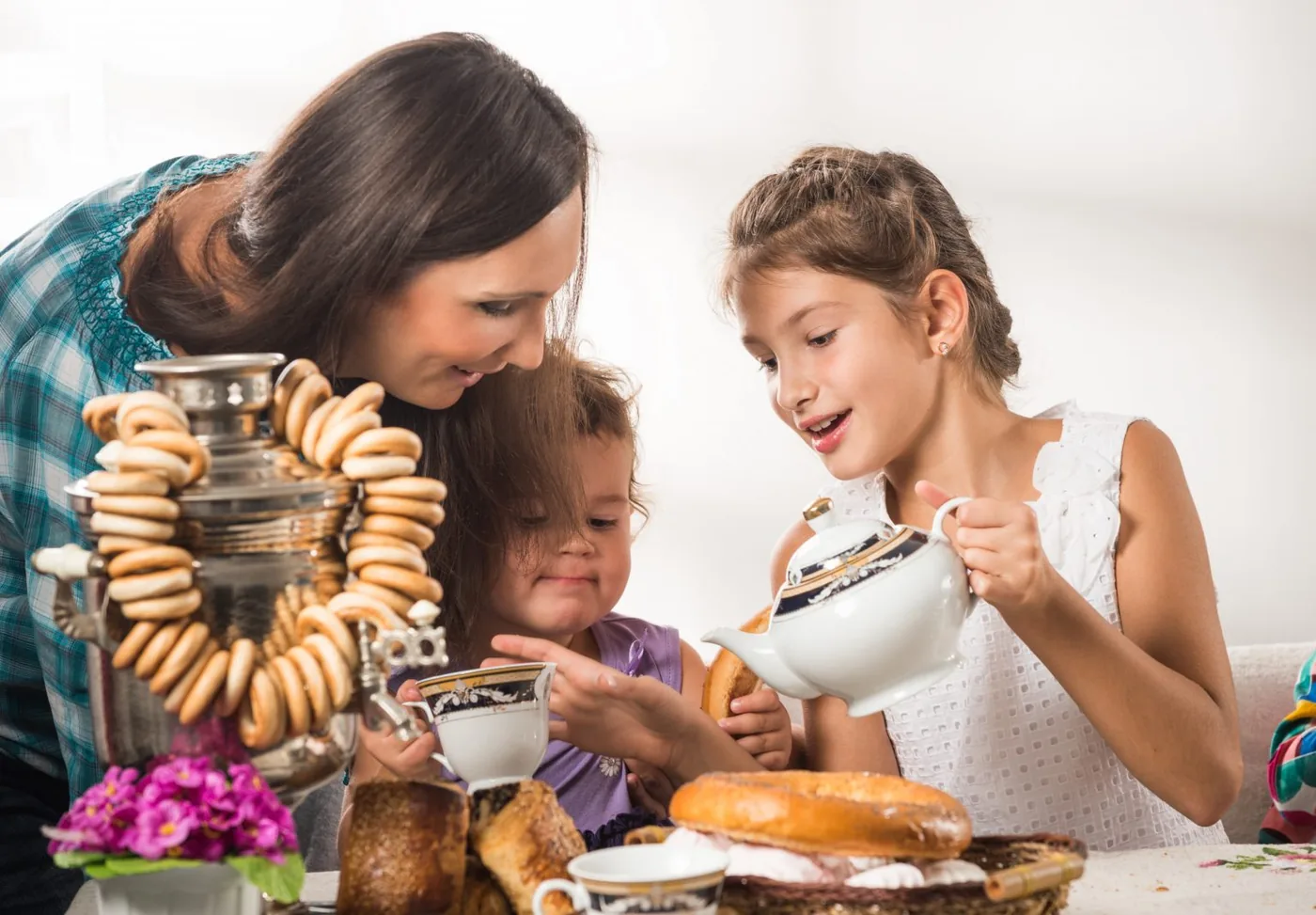 A mother and two daughters pouring tea from a samovar hung with dried bagels.