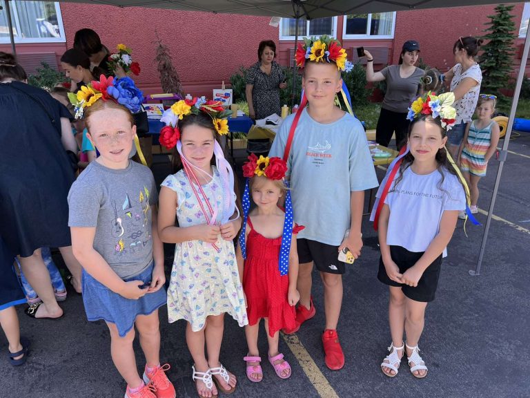 Five children with wreaths of flowers on their heads smiling at a Thrive International community event.